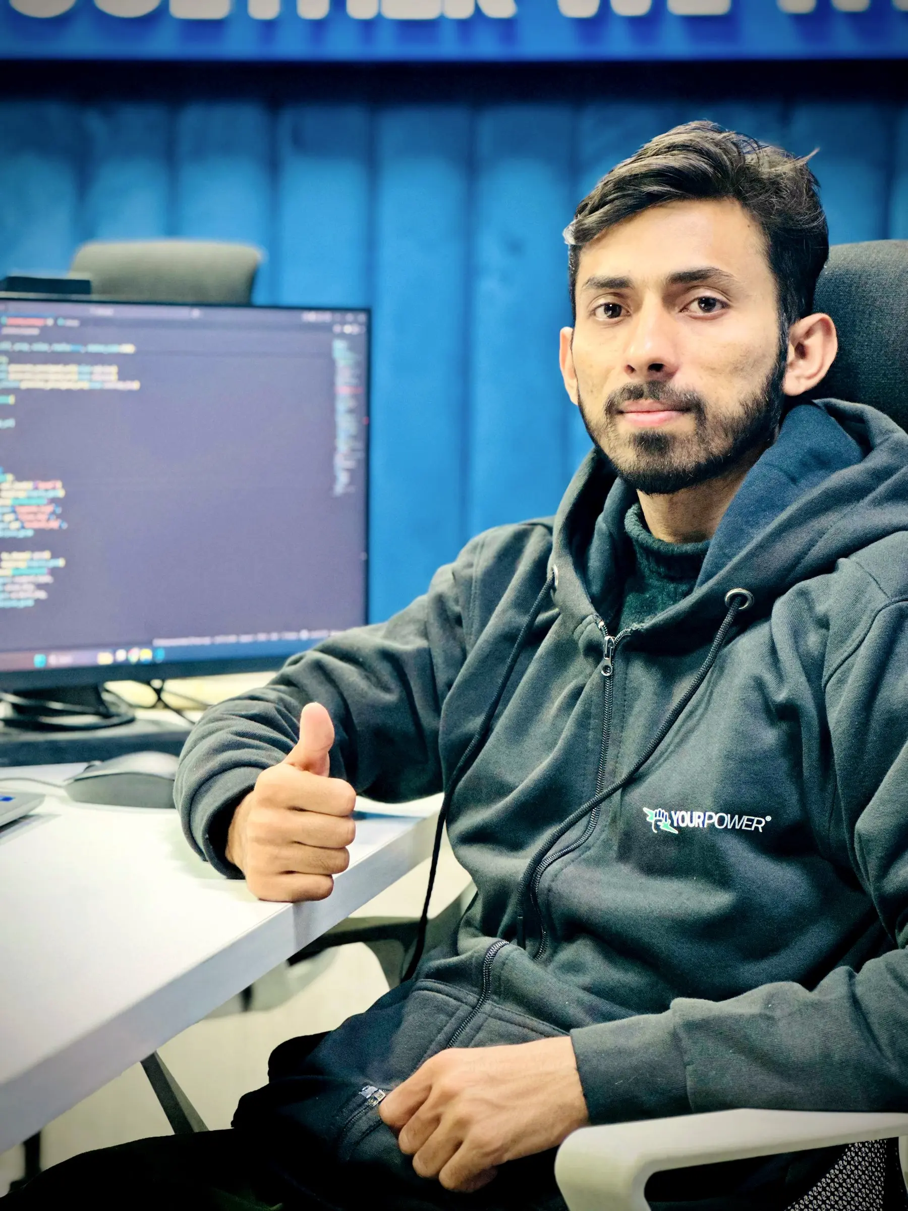 An engineer in a Your Power hoodie at his workstation, giving a thumbs up